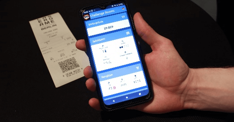 A hand holding a mobile phone displaying a mobile website, with a receipt featuring a QR code in the background