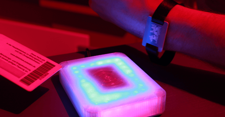 An arm with an RFID wristband approaching a lit reader