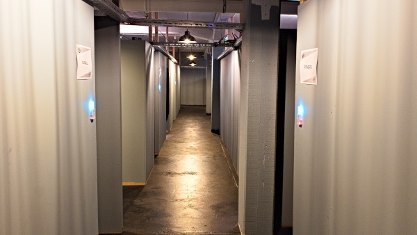 A corridor with grey walls and blue lights, leading to numbered rooms