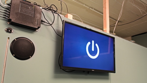 A wall-mounted screen showing a blue screen with a power symbol, next to a black control box with various cables and a speaker