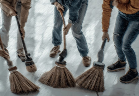 A drawing of four brooms on an ice surface, in front of three pairs of legs in blue trousers
