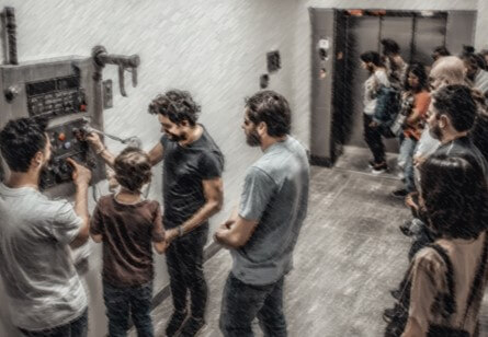A group of people in a hallway, some interacting with a control panel while others wait near an elevator