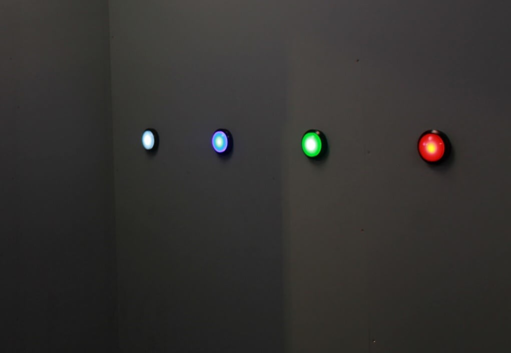 A wall with four large, round, glowing buttons in white, blue, green, and red