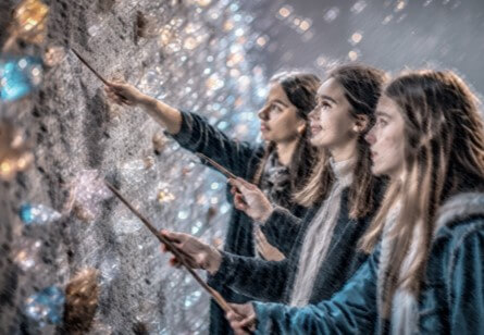 A group of people pointing magic wands at a textured wall adorned with sparkling lights and decorative elements
