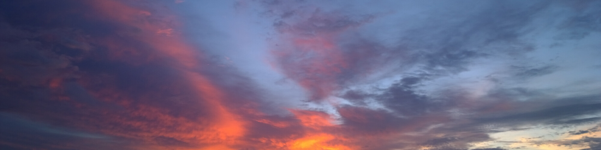 A panoramic view of a vibrant sunset sky, featuring shades of orange, pink, and purple clouds against a blue background